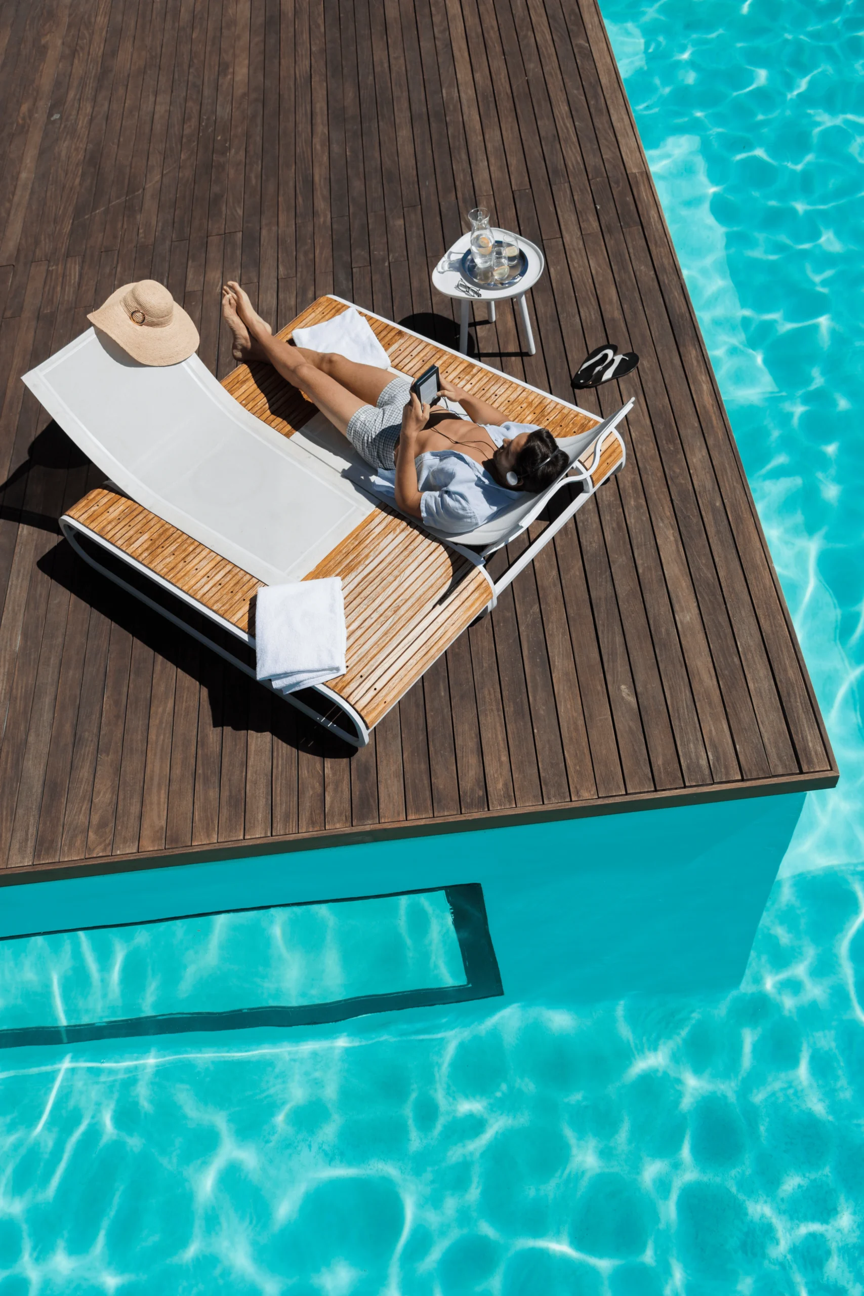 Relaxing by the Pool with a Book and Refreshing Drink Person relaxing by the pool, reading a book with headphones and a glass of water beside them