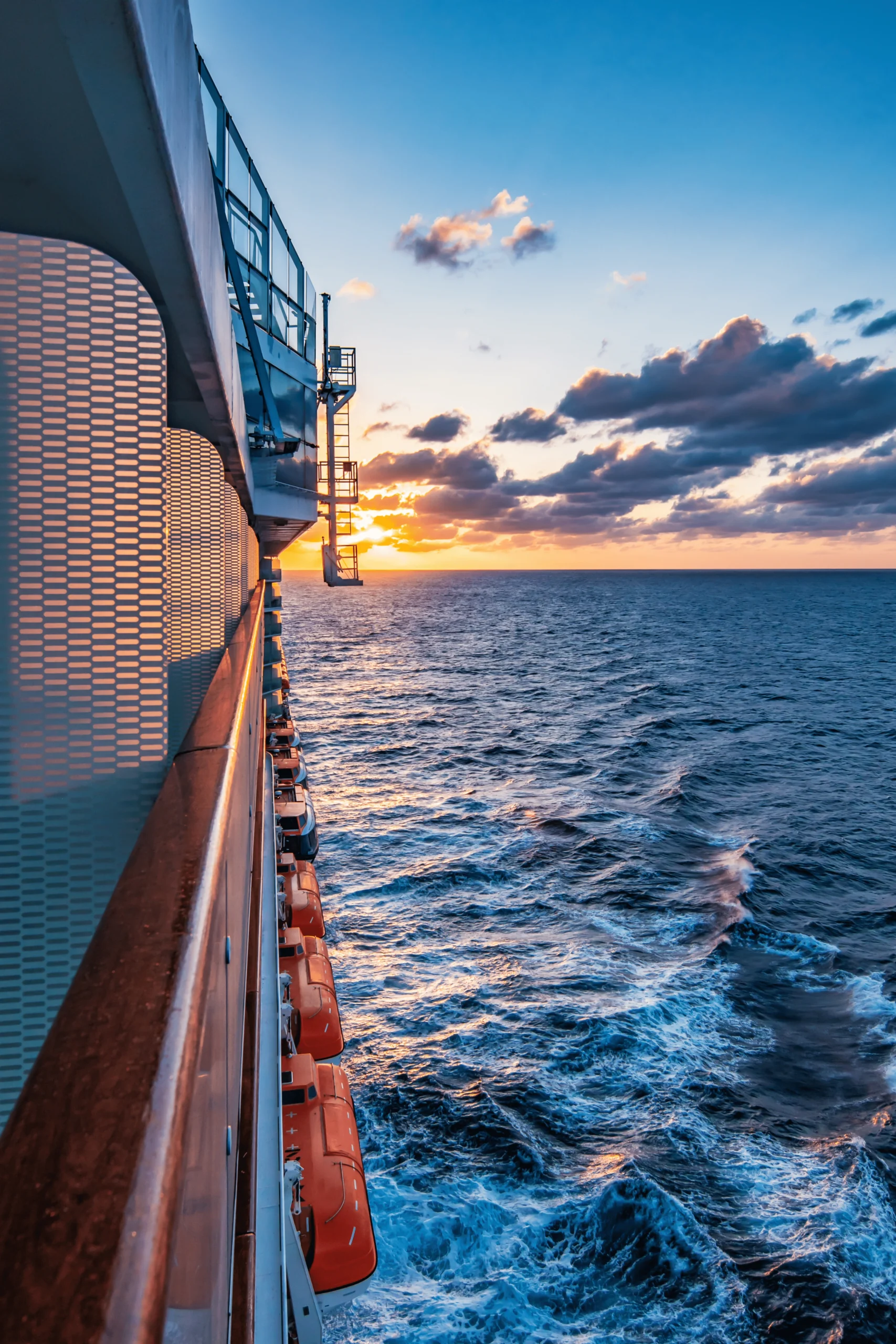Sunset View from a Cruise Ship View from a cruise ship at sunset, with the ocean and orange lifeboats visible against the sky.