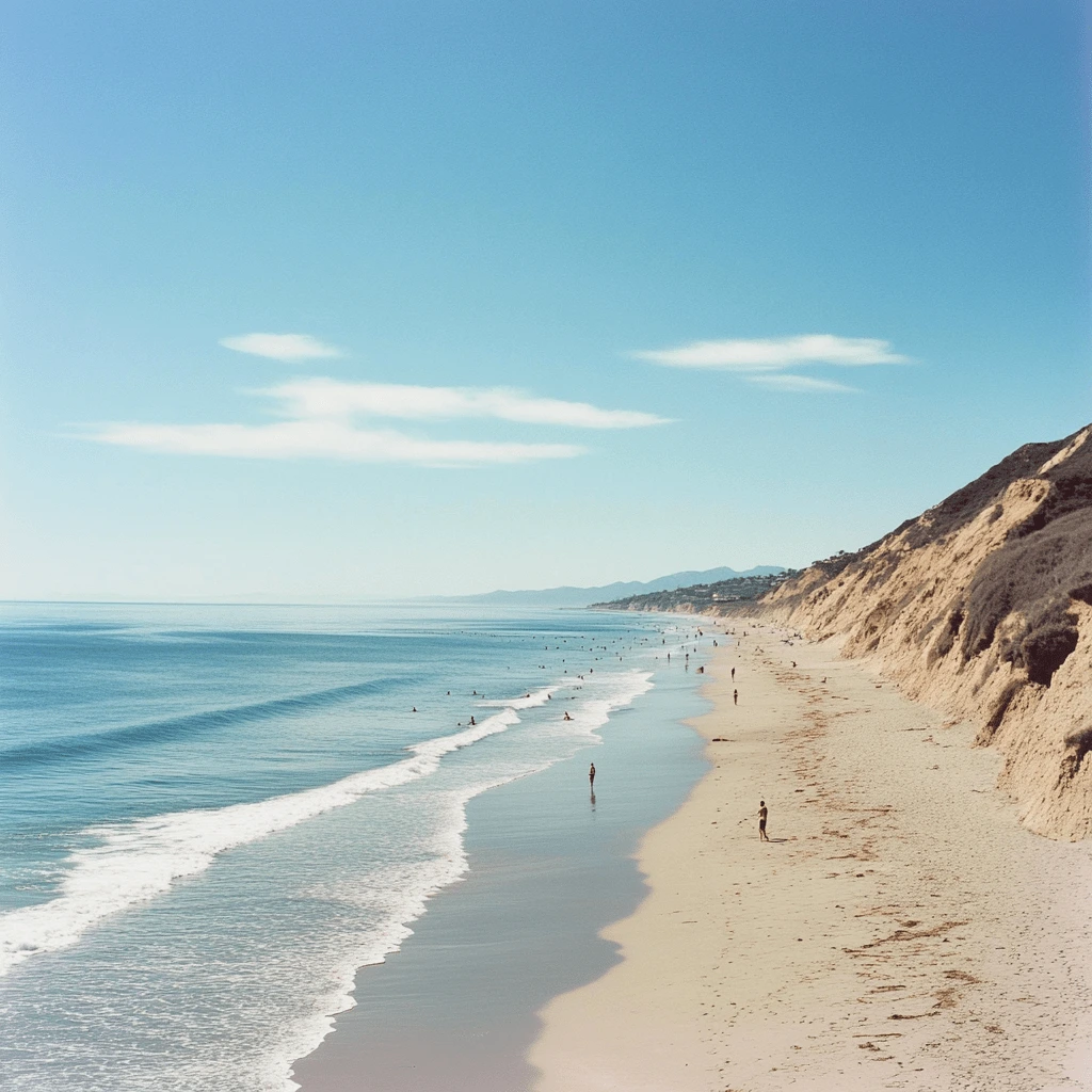 Zuma Beach in Malibu on a Clear Sunny Day Wide view of Malibu's Zuma Beach with golden sands, calm ocean waves, and a backdrop of cliffs under a bright blue sky.